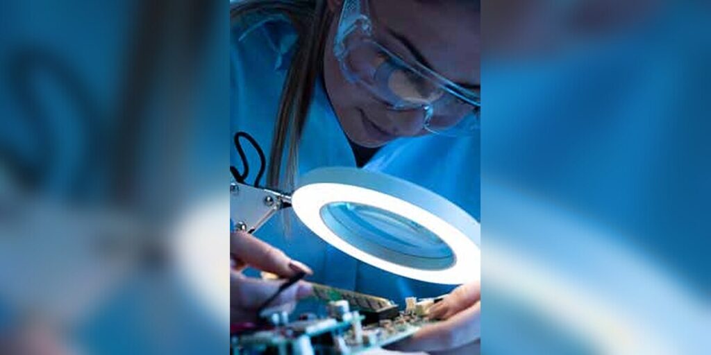 Técnica a reparar uma placa eletrónica sob uma lupa iluminada