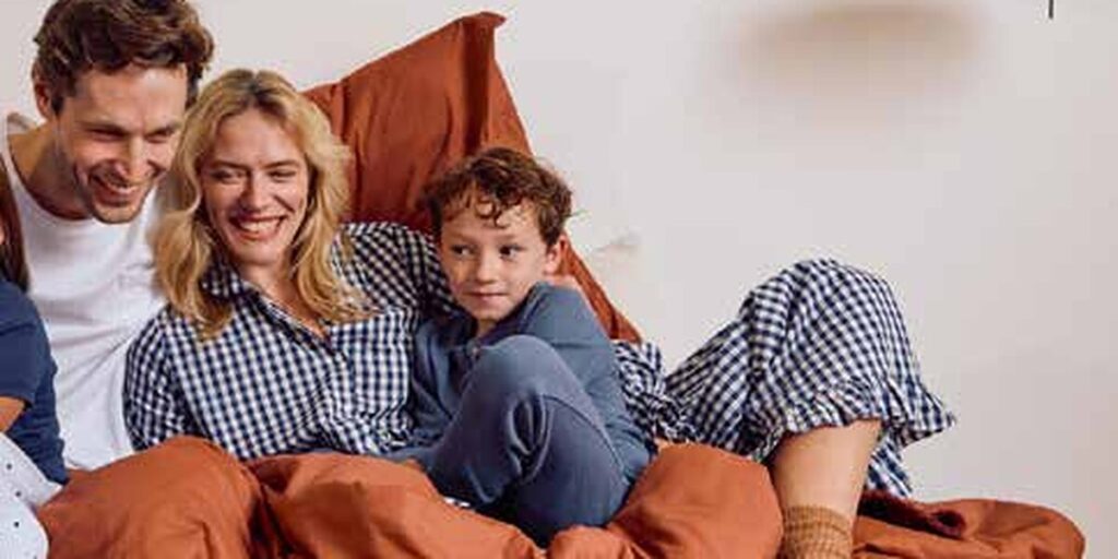 Família com duas crianças sentada numa cama, em roupa de dormir